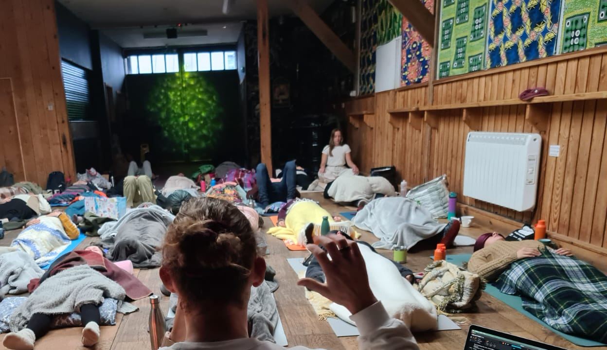 Joseph guiding a group breathwork session — a room of people lying down, deep in practice