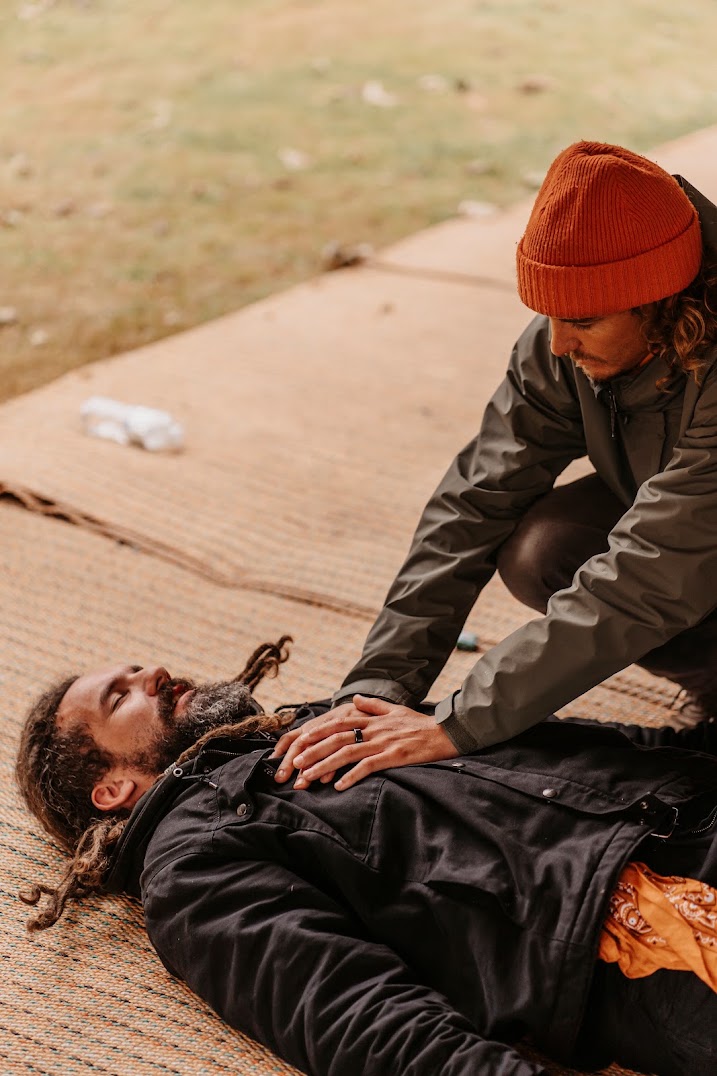 Joseph guiding a breathwork session outdoors, one hand resting on the chest of a man lying on mats